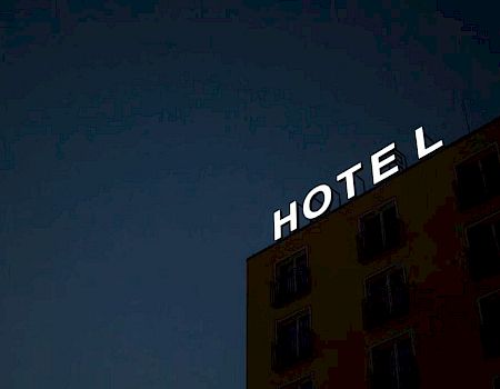 A building with a glowing sign that reads "HOTEL" at night. The sky is dark, and the building's windows are visible.