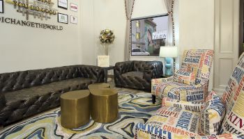 A cozy room with two dark sofas, colorful text-covered chairs, golden tables, and wall art stating 