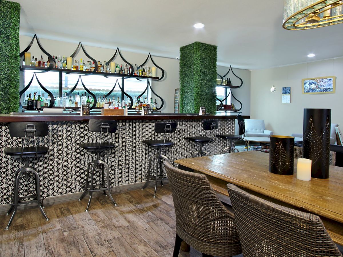 This image shows an elegantly designed bar area with high stools, decorative shelving, a wooden table, and candle-lit ambiance.