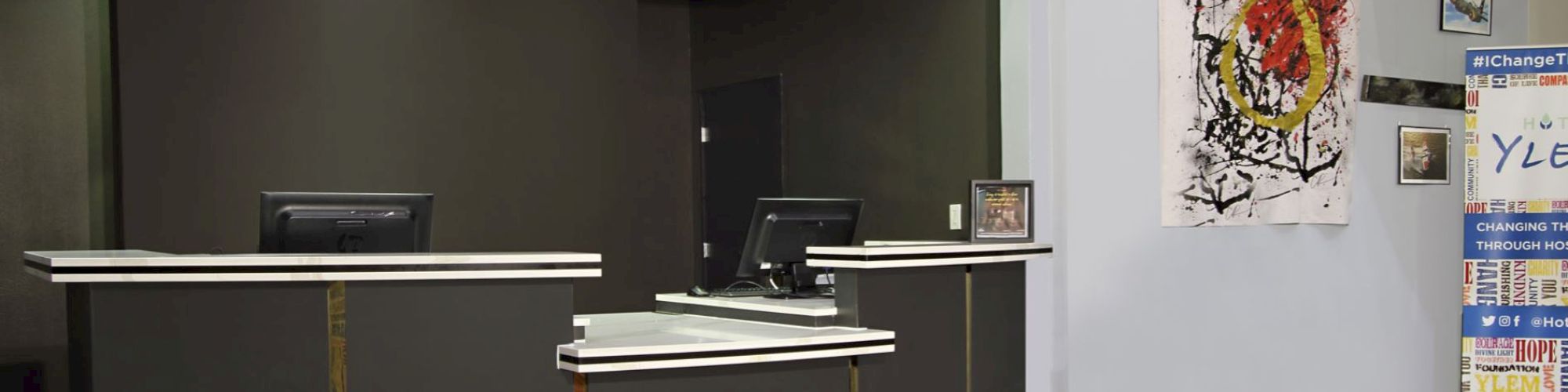 A reception desk area with two computer screens, abstract wall art, and a tall banner on the right side of the image.