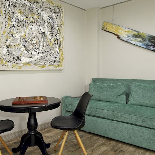 This image shows a modern room with abstract art on the walls, a green sofa, a round black table, and two black chairs.