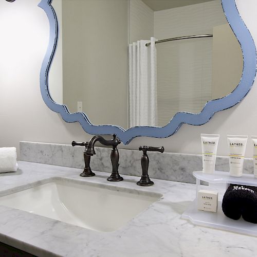 A bathroom sink with a marble countertop, toiletries, a towel, a decorative mirror, and a light fixture is visible in the image.