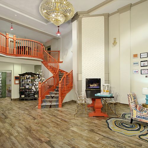 The image shows a spacious, modern interior with a wooden floor, an orange spiral staircase, seating area, wall decor, and a decorative chandelier.