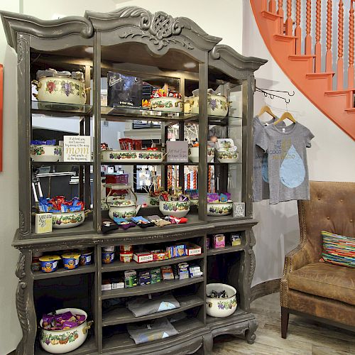 A cabinet with various items, a chalkboard, a brown chair with cushions, a grey t-shirt on a hanger, and an orange spiral staircase is visible.