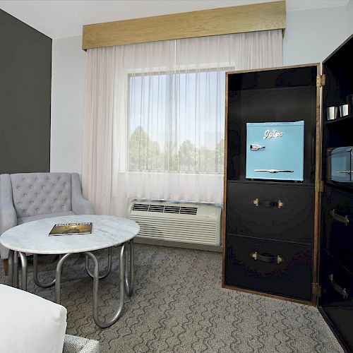 The image shows a modern hotel room with a bed, table, chair, cabinet, TV, microwave, curtain, and window, with a view of trees.