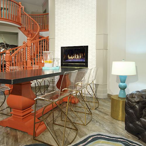 A modern living space with an orange staircase, black table, clear chairs, fireplace, leather sofa, and a unique lamp on a wooden floor.