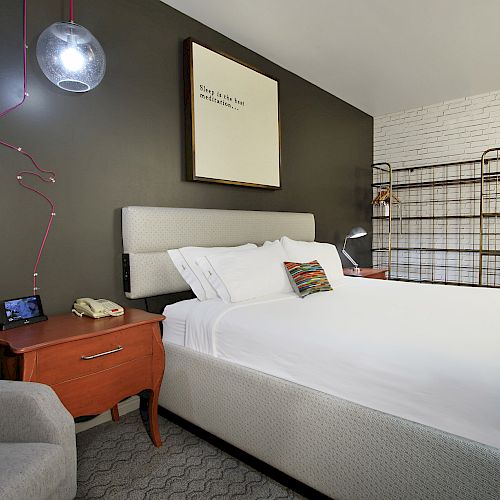 This image shows a modern hotel room with a white bed, a nightstand with a telephone and lamp, a gray chair, and minimalist decor, ending the sentence.