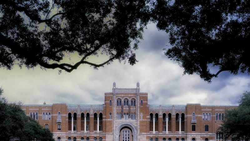 A large brick building with arched doors and columns, framed by trees.