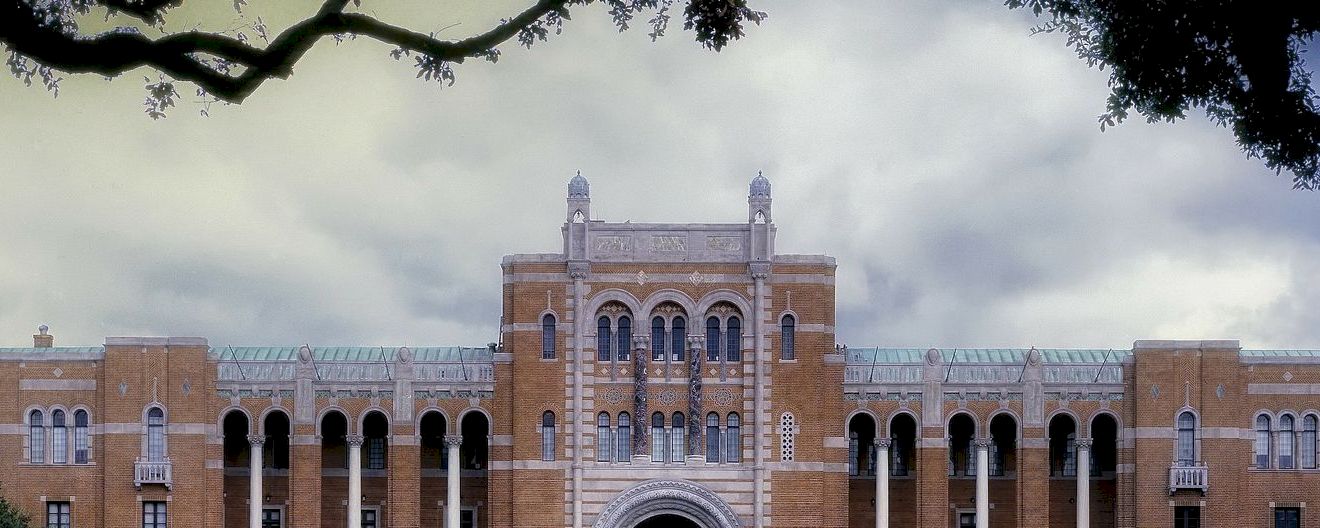 A large brick building with arched windows and columns under a cloudy sky.